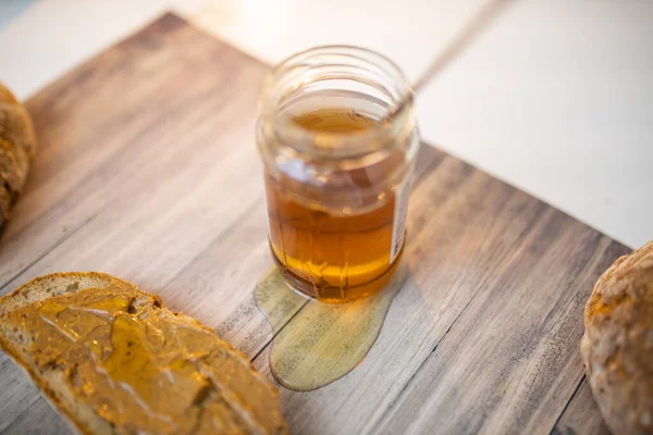 Honigglas und eine Scheibe Brot mit Erdnussbutter auf Holztisch — Stockfoto