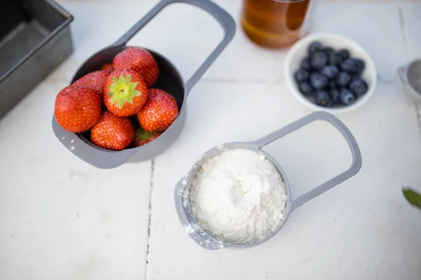 Morangos e farinha em copos de medição acima do balcão branco — Fotografia de Stock