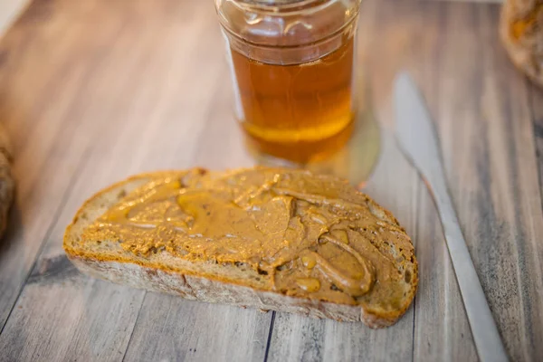 Tranche de pain au beurre d'arachide et pot de miel sur une table en bois — Photo