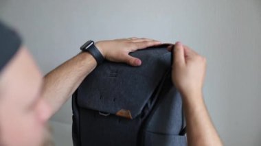 Adam gri bir sırt çantası ve fermuarını test ediyor.