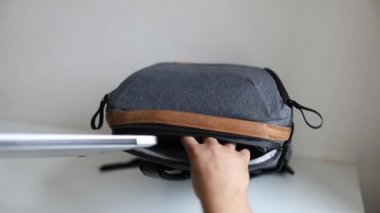 Erkek eller, gri bir sırt çantasının arka kompartımanında dizüstü bilgisayar taşıyor.