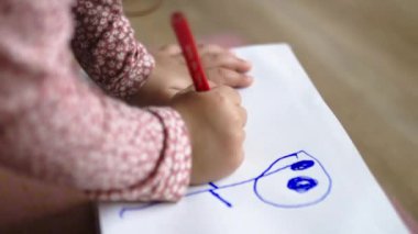 Küçük kız güzel bir şekilde kırmızı kalemle kağıda çiziyor.