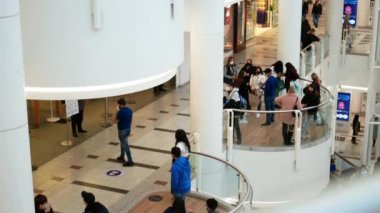 İnsanlar bir alışveriş merkezinin balkonunda kuyruğa giriyor.