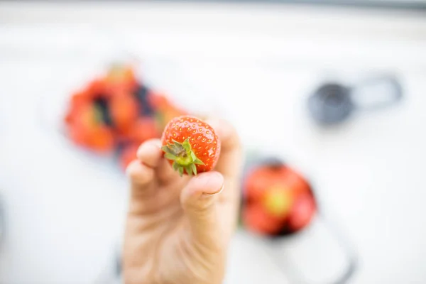 Mano femenina sosteniendo una fresa fresca por encima de más bayas —  Fotos de Stock