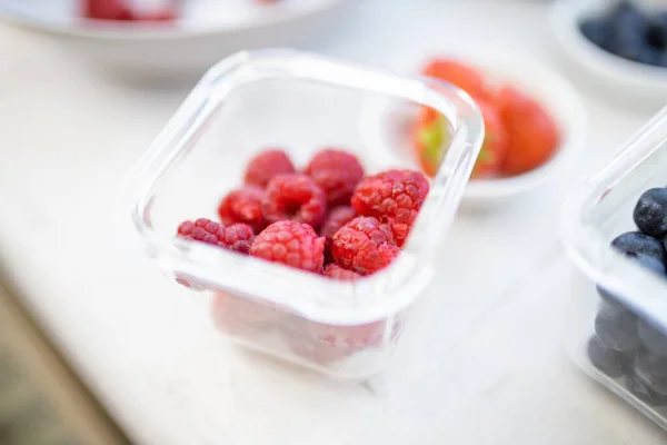 Frambozen in een plastic container op een witte tafel — Stockfoto