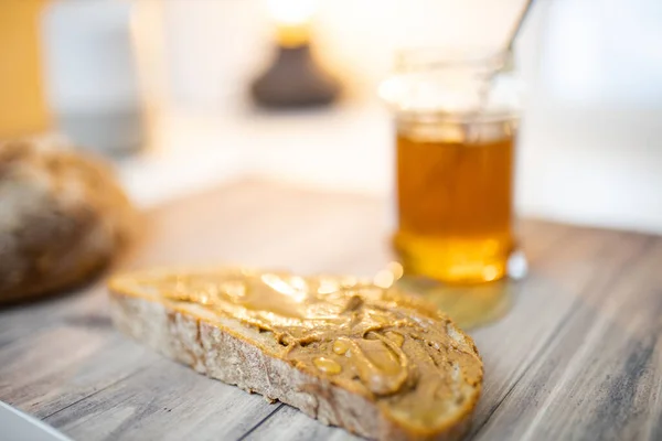 Fatia de pão com manteiga de amendoim e um pote de mel na mesa de madeira — Fotografia de Stock