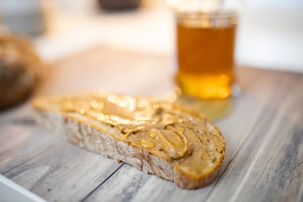 Fatia de pão com manteiga de amendoim e um pote de mel na mesa de madeira — Fotografia de Stock