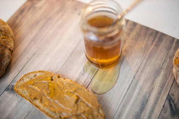Frasco de mel e uma fatia de pão com manteiga de amendoim na mesa de madeira — Fotografia de Stock