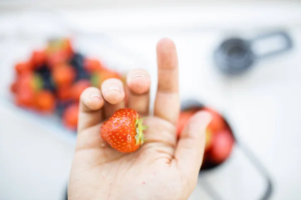 Fresa en una mano por encima de bayas borrosas en recipientes — Foto de Stock