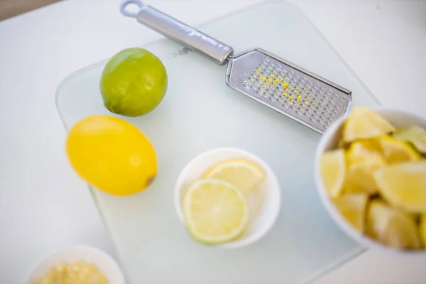 Чашки лаймов и лимонов на белом столе рядом с теркой — стоковое фото
