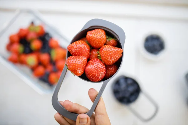 Taza medidora femenina llena de fresas por encima de más bayas —  Fotos de Stock