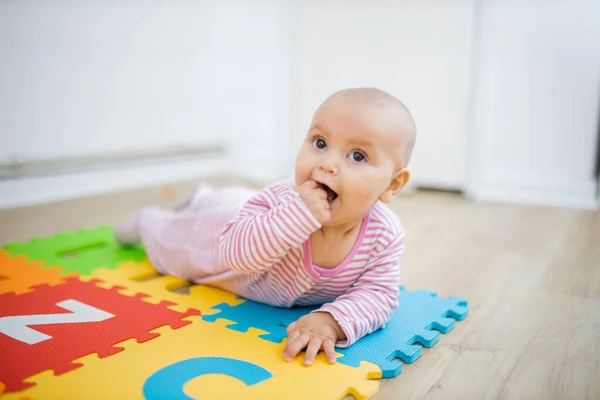 Schattige baby liggend op een kleurrijke mat met haar vuist in haar mond — Stockfoto