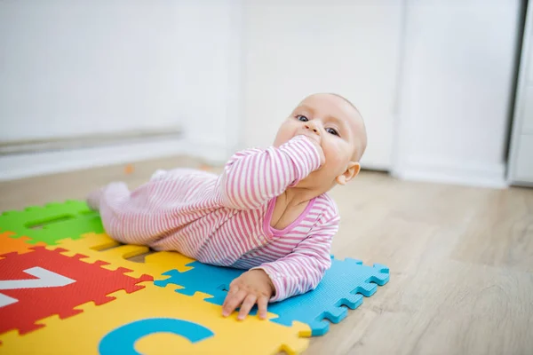 Schattige baby liggend op een kleurrijke mat met haar vuist in haar mond — Stockfoto