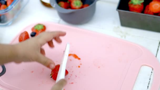 Manos femeninas cortando fresas en una tabla de cortar rosa — Vídeo de stock