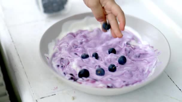 Mano femenina añadiendo arándanos a un tazón de yogur — Vídeo de stock