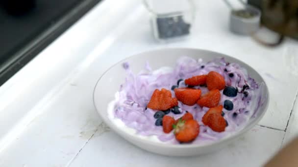 Tangan wanita menambahkan strawberryies ke dalam mangkuk yogurt — Stok Video