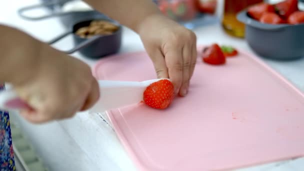 Vrouwelijke handen snijden aardbeien op een roze snijplank — Stockvideo