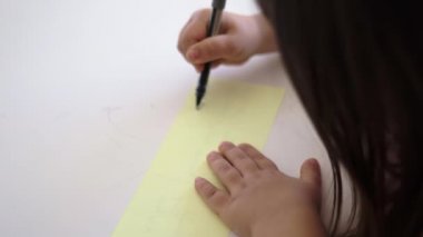 Küçük kız bir kağıt parçasına çiziyor ve bir kutuya koyuyor.