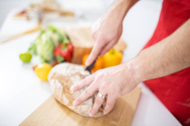 Erkek eli kesme tahtasının üzerinde ekmek kesiyor.