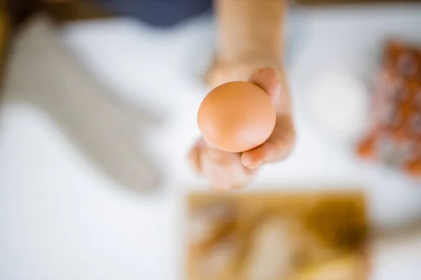 Female hand holding an egg above ingredients on a table — Stock Photo, Image