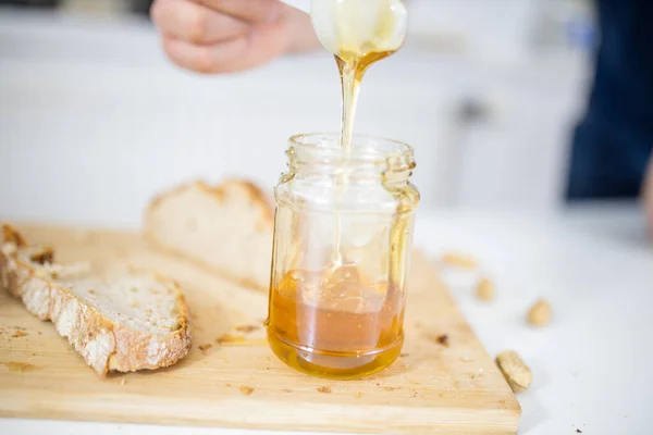 Mužská ruka sbírá med ze sklenice vedle krajíčku chleba — Stock fotografie