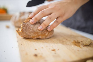 Kesme tahtasında ekmek dilimleyen kadın elleri.