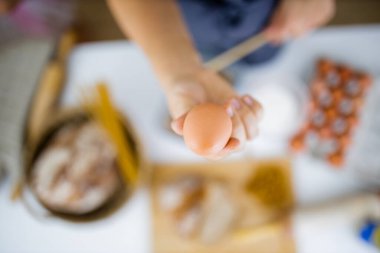Masadaki malzemelerin üstünde yumurtayı tutan bir kadın.