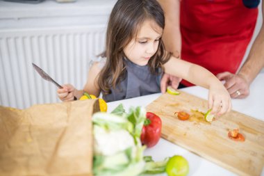 Küçük kız ve babası kesme tahtasında sebze doğruyor.
