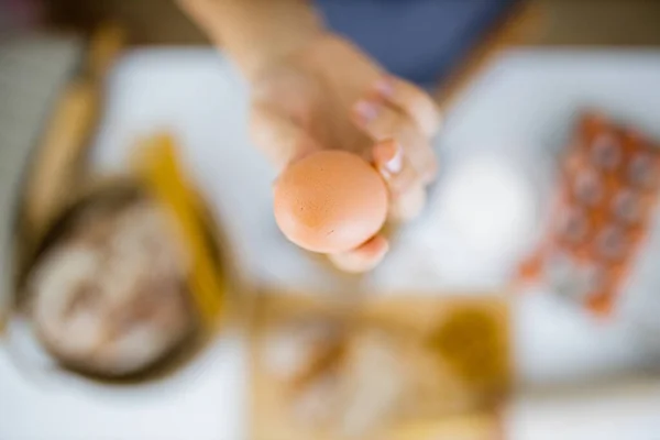 Female hand holding an egg above ingredients on a table — Stock Photo, Image