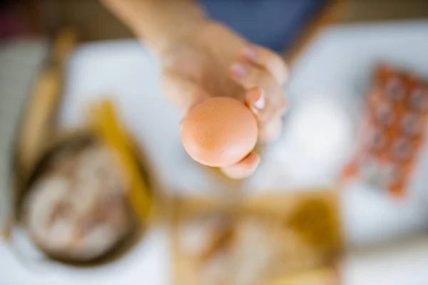 Tangan wanita memegang telur di atas bahan-bahan di atas meja — Stok Foto