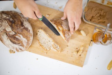 Kesme tahtasında ekmek dilimleyen kadın elleri.