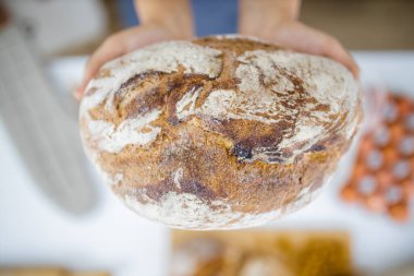 Masadaki malzemelerin üzerinde ekmeği tutan kadın elleri.