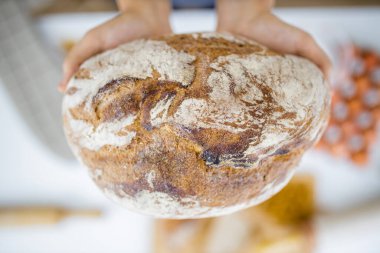 Masadaki malzemelerin üzerinde ekmeği tutan kadın elleri.
