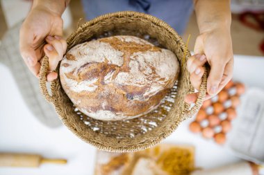 Masadaki malzemelerin üstündeki sepette ekmeği tutan kadın elleri.