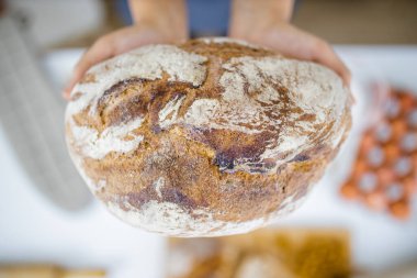 Masadaki malzemelerin üzerinde ekmeği tutan kadın elleri.