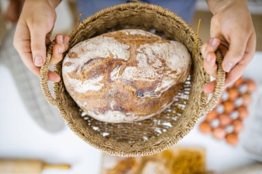 Masadaki malzemelerin üstündeki sepette ekmeği tutan kadın elleri.