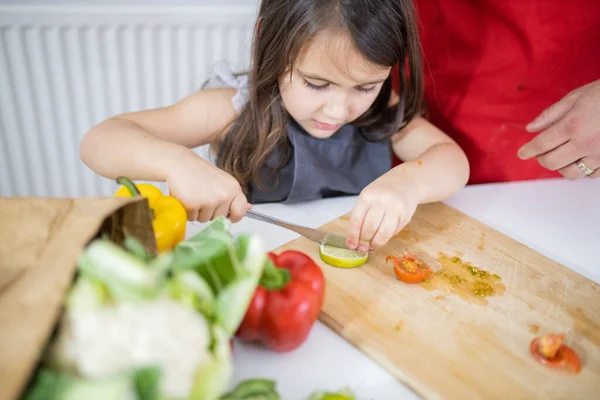 Niña y su padre cortando verduras en una tabla de cortar — Foto de Stock