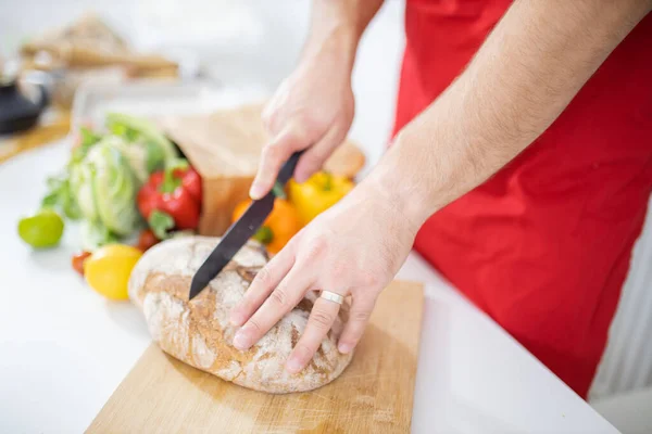 Mãos masculinas cortando pão em uma tábua de corte — Fotografia de Stock