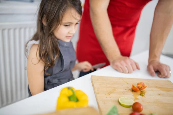 Klein meisje en haar vader snijden groenten op een snijplank — Stockfoto