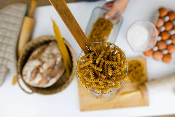 Okokt fusilli på träpasta sil ovanför ingredienser på ett bord — Stockfoto