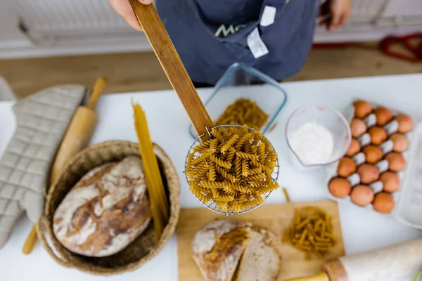 Ongekookte fusilli op houten pasta zeef boven ingrediënten op een tafel — Stockfoto