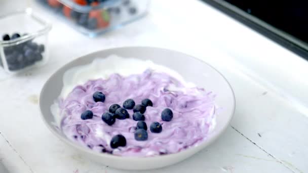 Main féminine ajoutant des bleuets dans un bol de yaourt — Video