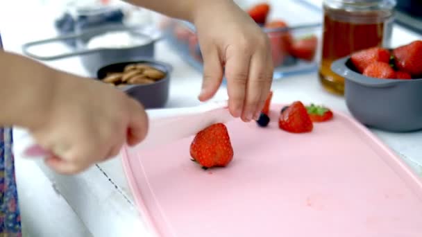 Manos femeninas cortando fresas en una tabla de cortar rosa — Vídeo de stock