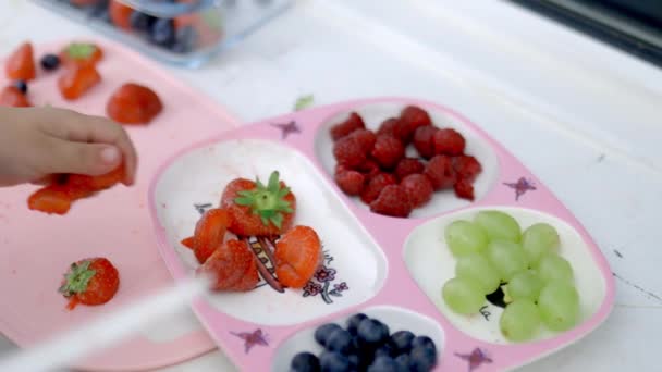 Weibliche Hände schneiden Erdbeeren und legen sie auf ein rosafarbenes Tablett — Stockvideo