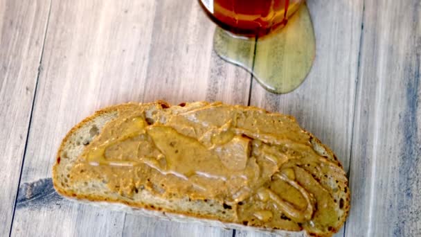 Rebanada de pan con mantequilla de maní y un tarro de miel en la mesa de madera — Vídeos de Stock