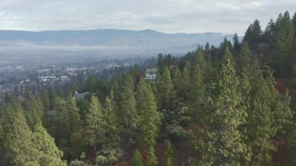 Πετώντας πάνω από δέντρα και σπίτια σε ένα λόφο με Majestic βουνά ως φόντο — Αρχείο Βίντεο