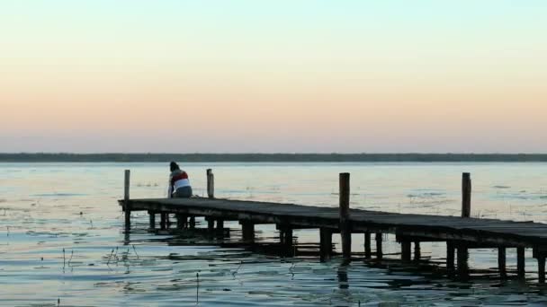 4k Prise de vue d'un quai dans le lac Bacalar avec une femme assise sur le bord au coucher du soleil — Video