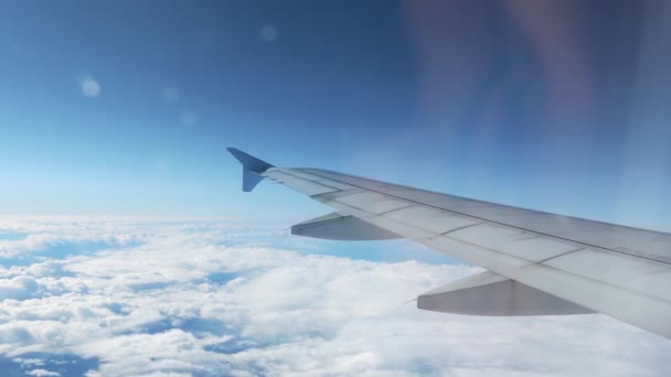 4k Aufnahme eines über den Wolken fliegenden Flugzeugflügels mit blauem Himmel als Hintergrund — Stockvideo