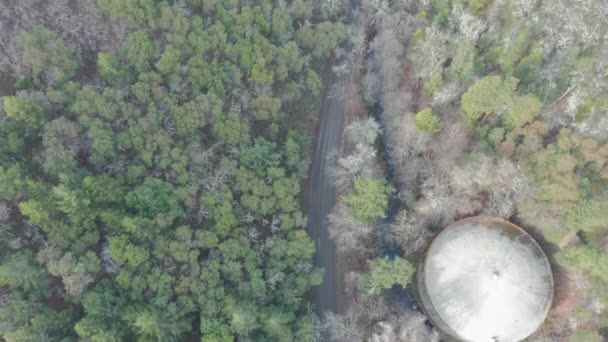 4k vista aérea segue uma estrada cercada pela floresta para descobrir uma cidade pequena e uma montanha — Vídeo de Stock