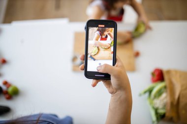 Akıllı telefonlu bir kadın, avokado kesen küçük bir kızı kaydediyor.